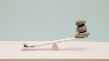 Image of small scale seesaw with feather on one end and three stacked rocks on the other end.
