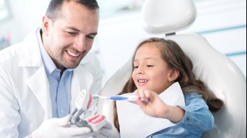 Dentists teaching a child how to brush their teeth. He is holding a mold, the child has a toothbrush. 